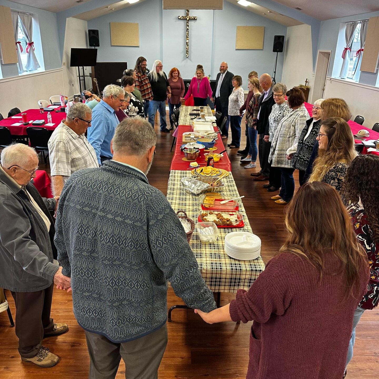 group of people holding hands praying around a table of pot luck food